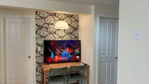 Ein Zimmer mit Fernseher an der Wand, einem Holztisch mit Stühlen und einer Tür.