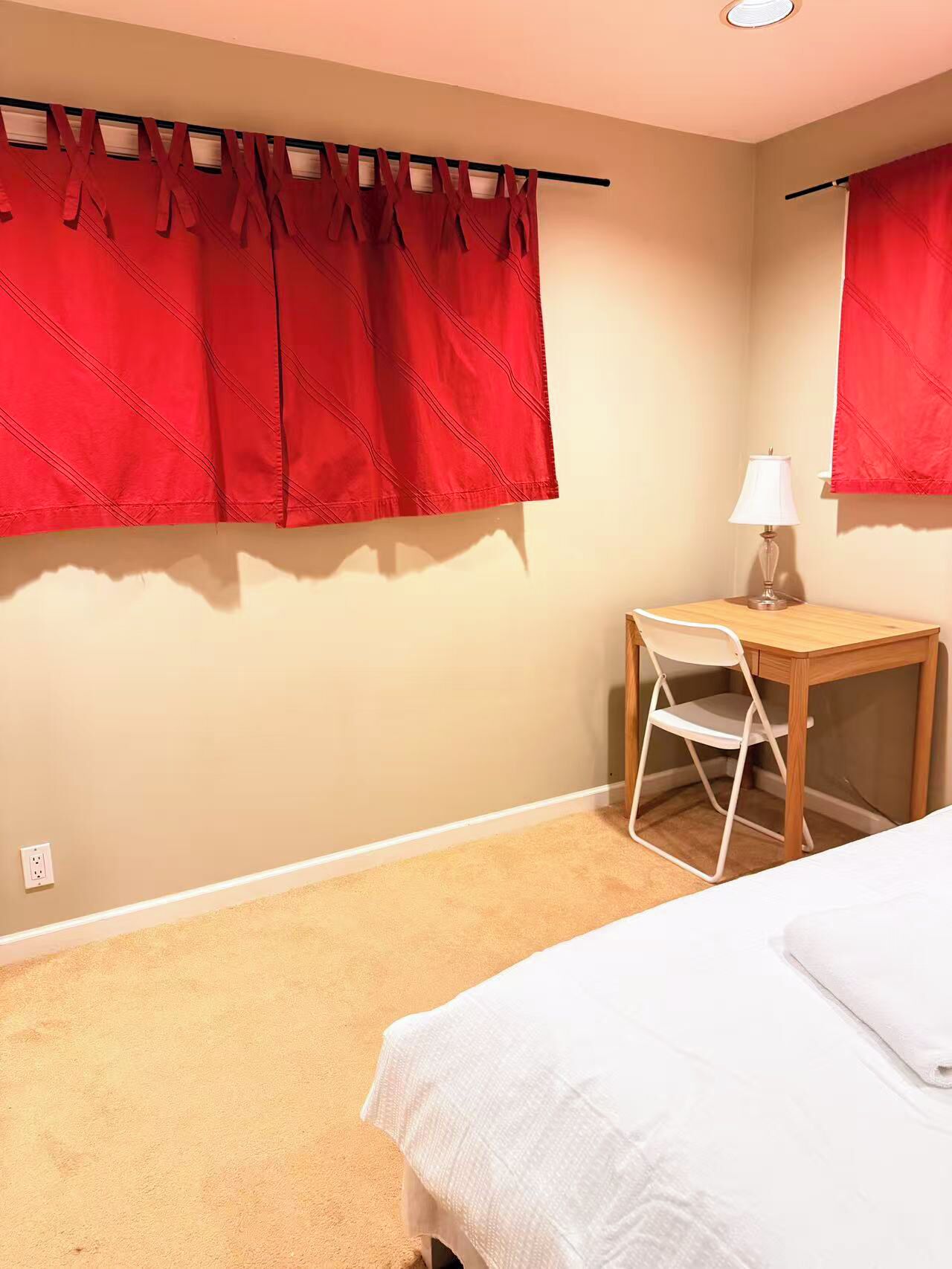 Quarto com cama, escrivaninha com cadeira, luminária e cortinas vermelhas.