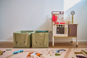 Un área de juegos para niños con una cocina de juguete, contenedores de almacenamiento y una alfombra estampada.