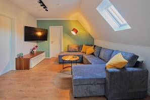 Un loft moderno con un gran ventanal, un sofá modular, una pequeña mesa redonda de centro y un televisor de pantalla plana montado en la pared.