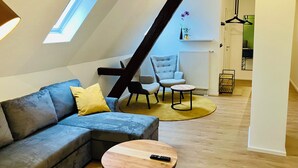 Moderni loft-tyylinen asunto, jossa on kalteva katto, kulmasohva, harmaa nojatuoli, pieni pyöreä pöytä ja riippuvalaisin.