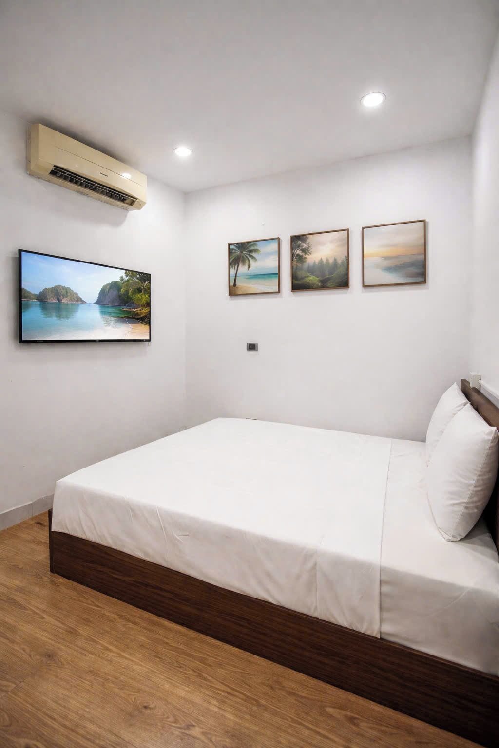 A bedroom with a bed, a wall-mounted air conditioner, and three framed landscape paintings.