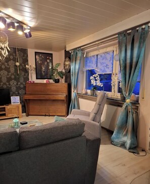 A living room with a sofa, a piano, a television, and a window with curtains. - Vacation apartment Seeblick in Langweiler (Langweiler)