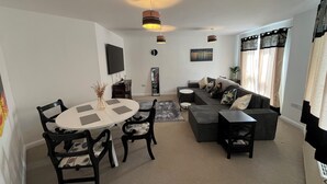 A modern living room with a dining area, a sofa set, a TV, and a ceiling fan. - Perfect Spacious & Comfortable 2-bedroom Apartment in Derby for a relaxing stay (Derby)