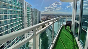 A balcony with a glass railing, a chair, and a view of the cityscape.