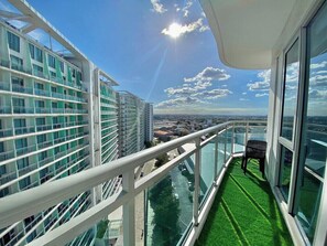 A balcony with a glass railing, a chair, and a view of the cityscape.