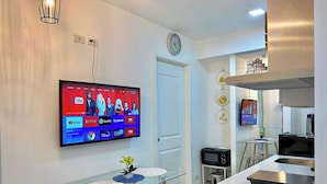A modern kitchen with a flat-screen TV, a glass dining table, and a microwave.