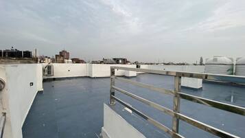 A rooftop terrace with a metal railing, flat roof, and distant cityscape.