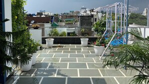 Terraço no telhado com plantas em vasos, estrutura metálica e vista para a cidade.