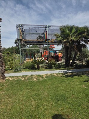 Un parque infantil con una estructura de escalada con red, palmeras y un sendero.