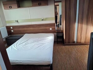 A hotel room with a bed, a small table, a mirror, and a wardrobe. - Mobilhome in a 3* campsite in argeles sur mer sleeps 6 (Argelès-sur-Mer)