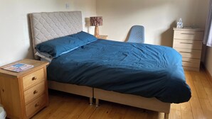 Un dormitorio con cama, mesita de noche, lámpara, silla, cómoda y un cuadro en la pared.