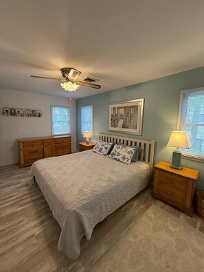 A bedroom with a bed, wooden dresser, nightstands, a ceiling fan, and a framed picture on the wall. - Bethany Victorian Short Walk to the Beach with Wooded Yard (Bethany Beach)