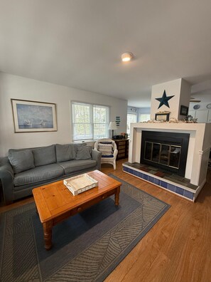 A living room with a fireplace, a sofa, a coffee table, and a framed picture on the wall. - Bethany Victorian Short Walk to the Beach with Wooded Yard (Bethany Beach)