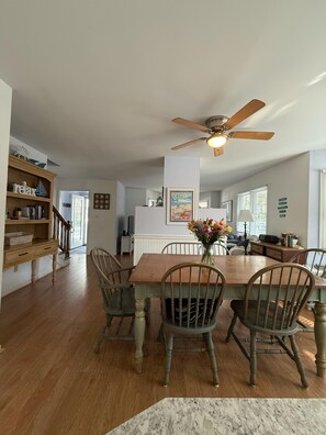 A dining area with a wooden table, four chairs, a ceiling fan, and a vase with flowers. - Bethany Victorian Short Walk to the Beach with Wooded Yard (Bethany Beach)