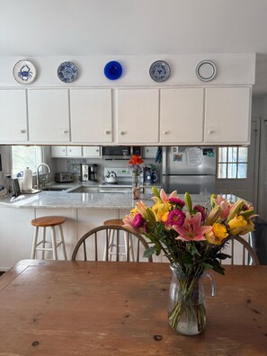 Uma cozinha com armários brancos, uma mesa de jantar com um vaso de flores e um prato decorativo azul na parede.