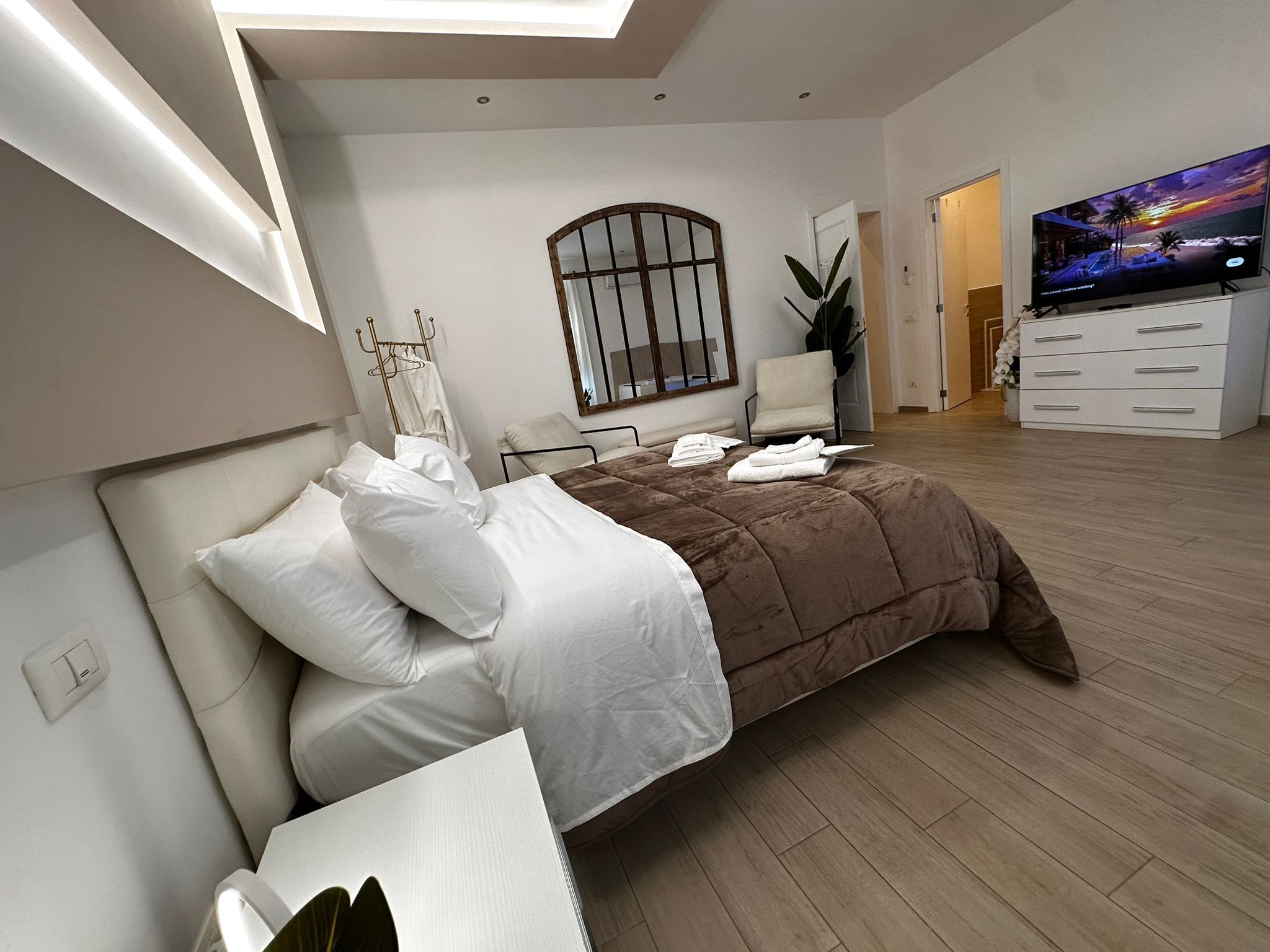 Un dormitorio moderno con una cama, un televisor, un aparador y un ventanal grande.