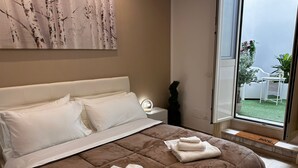 Et soveværelse med en stor seng, et natbord med en lampe, et vindue der ud til en have, og en dør.