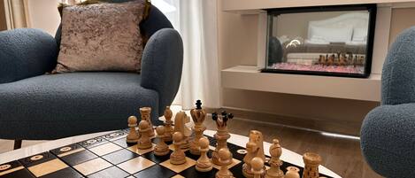 A chessboard with pieces set up on a table in a living room with a sofa and a fireplace.