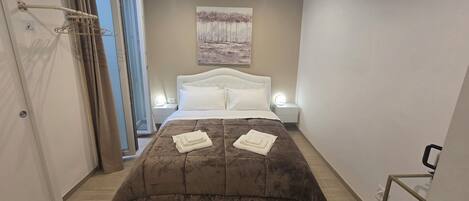 A bedroom with a bed, bedside lamps, a painting on the wall, and a bathroom with a toilet and sink.