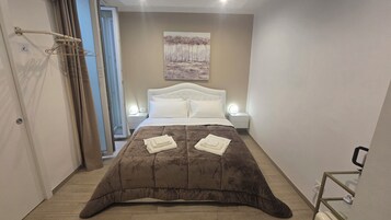 Un dormitorio con cama, lámparas de noche, un cuadro en la pared y un baño con inodoro y lavamanos.