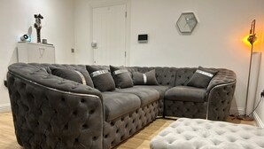 A sectional sofa with a chaise, a matching ottoman, a floor lamp, a clock, and a small cabinet with decorative items.