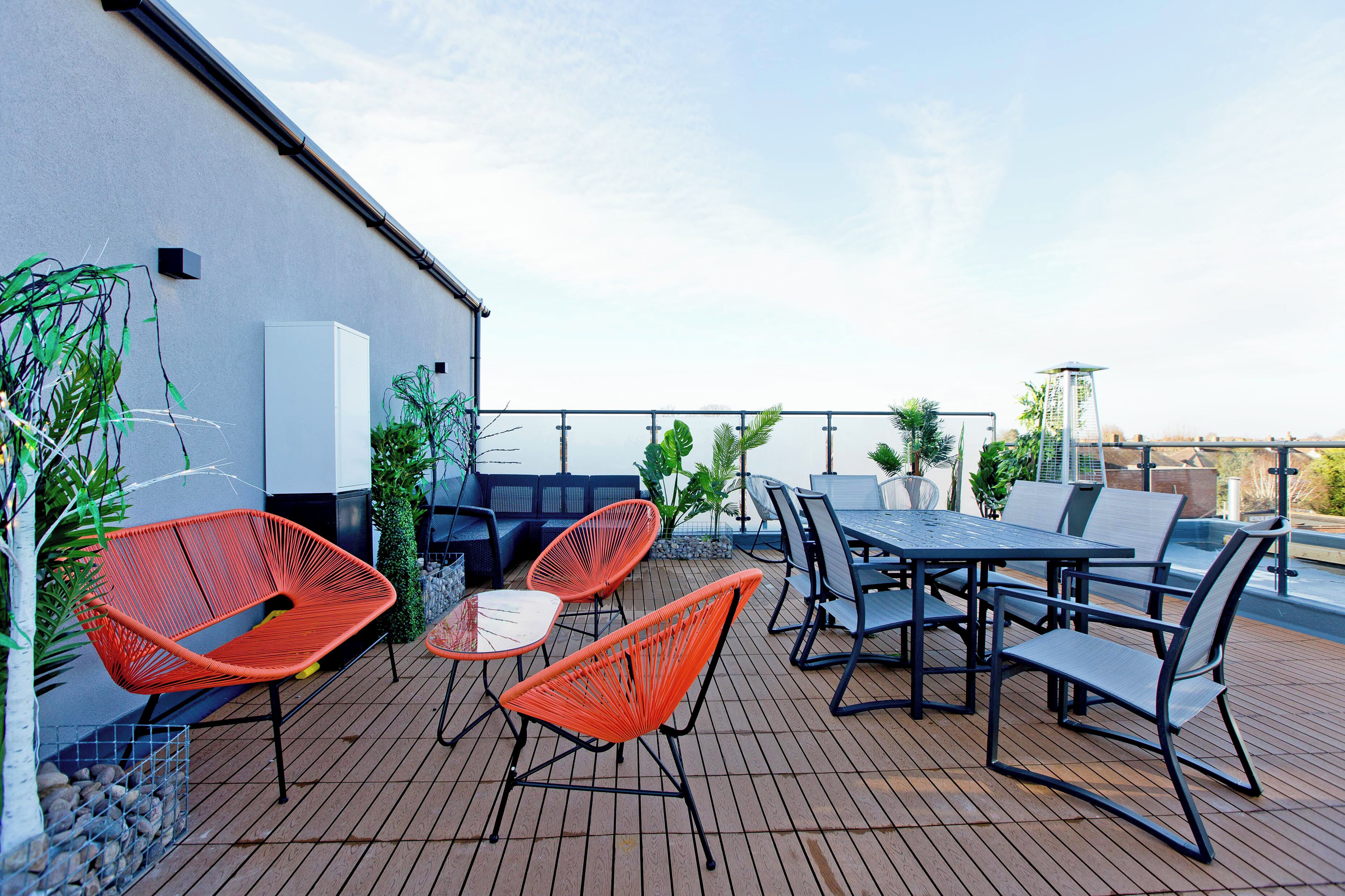 An outdoor patio with a table and chairs, a white wall, and potted plants.