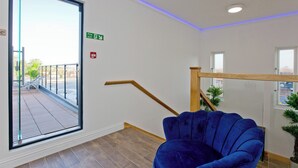 A room with a blue chair, a wooden staircase, a glass door leading outside, and a green exit sign.