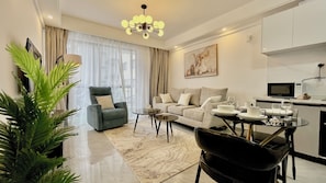A modern living room with a sofa, armchair, coffee table, and dining table set with plates and glasses. - Cozy 1-bedroom apartment in marvelous Nairobi Westlands with Pool and gym access (Nairobi)