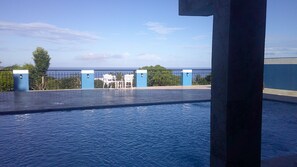 A swimming pool with a view of the sea, a white chair, and a blue and white building in the background.