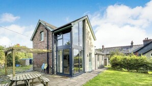 Ein modernes Haus mit großem Glasanbau, einer Holzpergola und einer gepflasterten Terrasse.