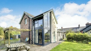 Ett modernt hus med en stor glasveranda, en träpergola och en stenlagd uteplats.