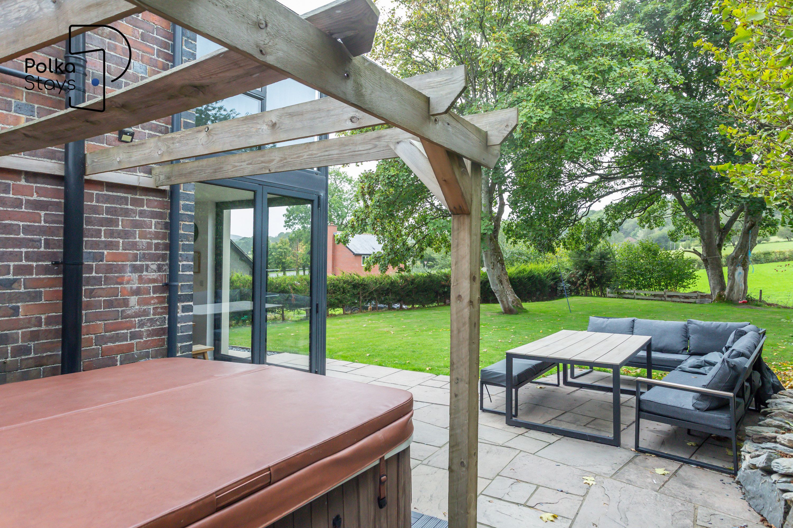 Ein Außenbereich mit einer Holzpergola, einer Ziegelwand und einer Glastür, die zu einem Garten führt.
