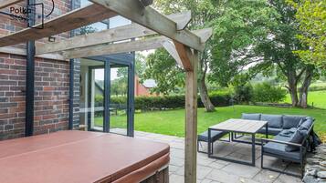 Ein Außenbereich mit einer Holzpergola, einer Ziegelwand und einer Glastür, die zu einem Garten führt.