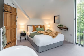A modern bedroom with a large bed, bedside lamps, a mirror, and a view of greenery outside.