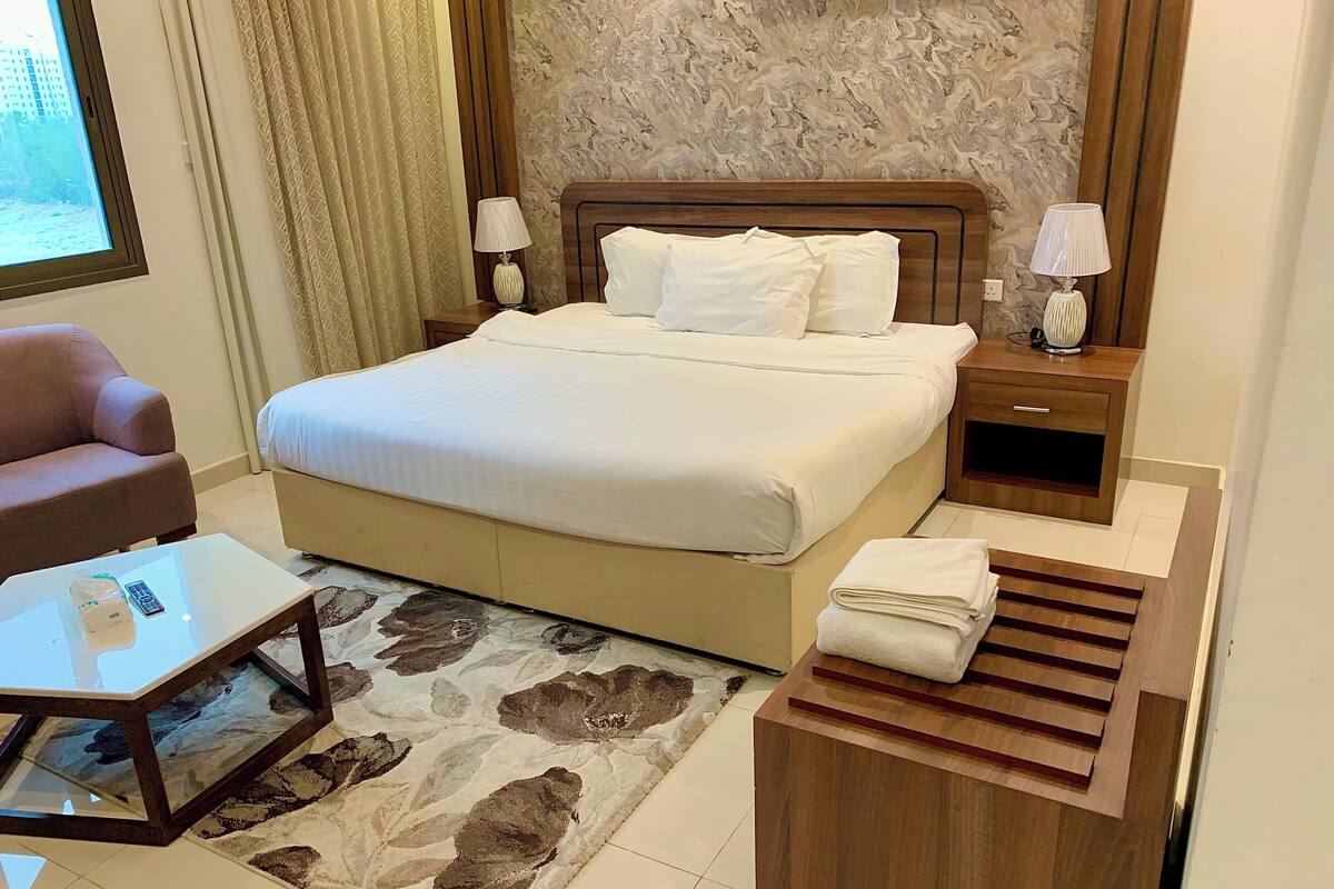 Una habitación de hotel con una cama, una mesita de noche, una silla, una alfombra y una ventana.