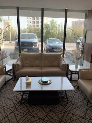 A modern lobby with a leather sofa, a marble coffee table, and large windows offering a view of parked cars and buildings. - qamar albahr (Al Khobar)