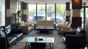 A modern lobby with leather sofas, a coffee table, and large windows offering a view of parked cars outside. - qamar albahr (Al Khobar)
