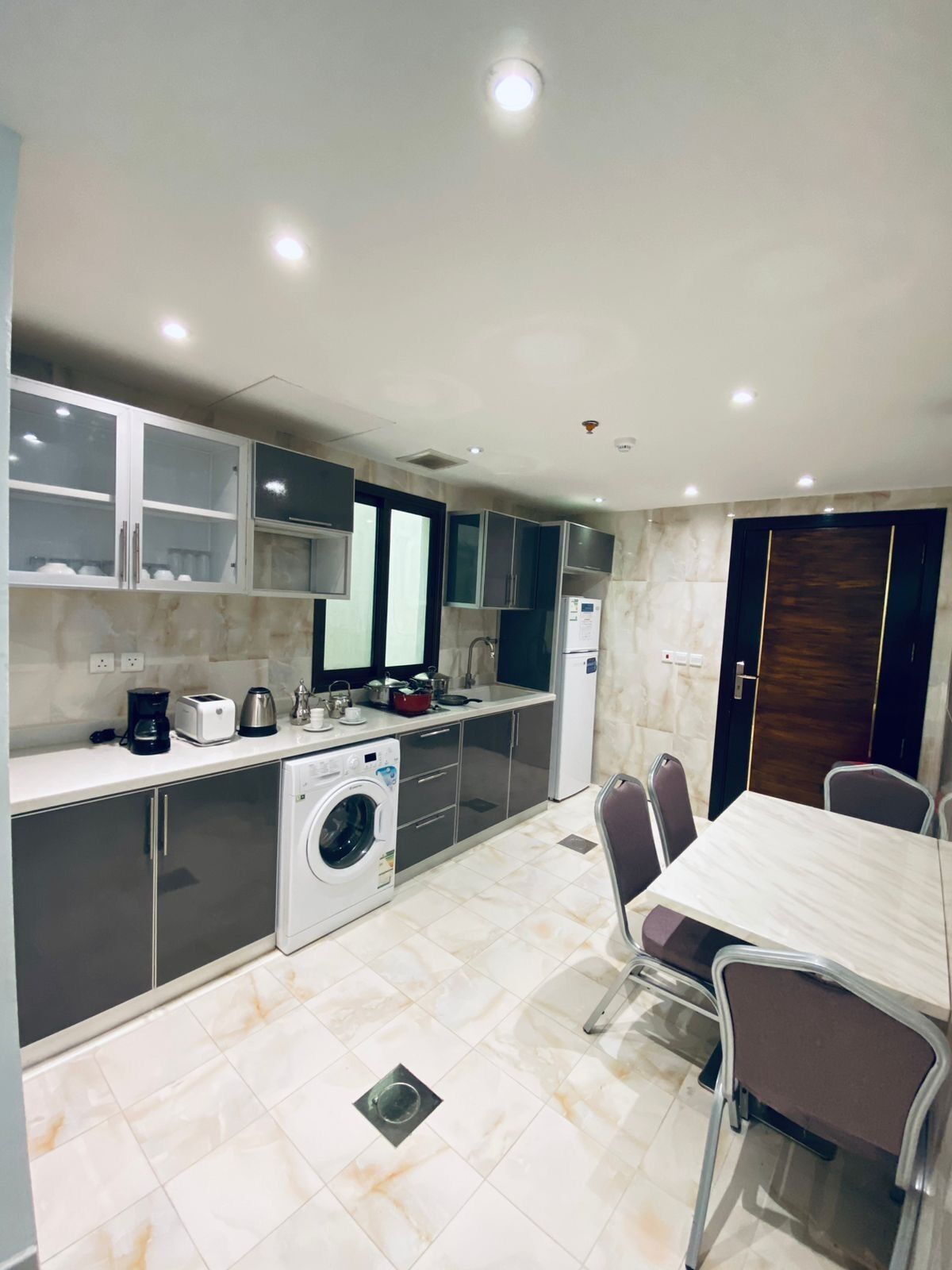 A compact kitchen with a washing machine, a dining table, and chairs.