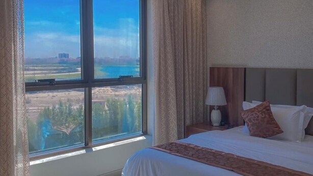 A hotel room with a large window, a bed, a nightstand, and a lamp. - qamar albahr (Al Khobar)