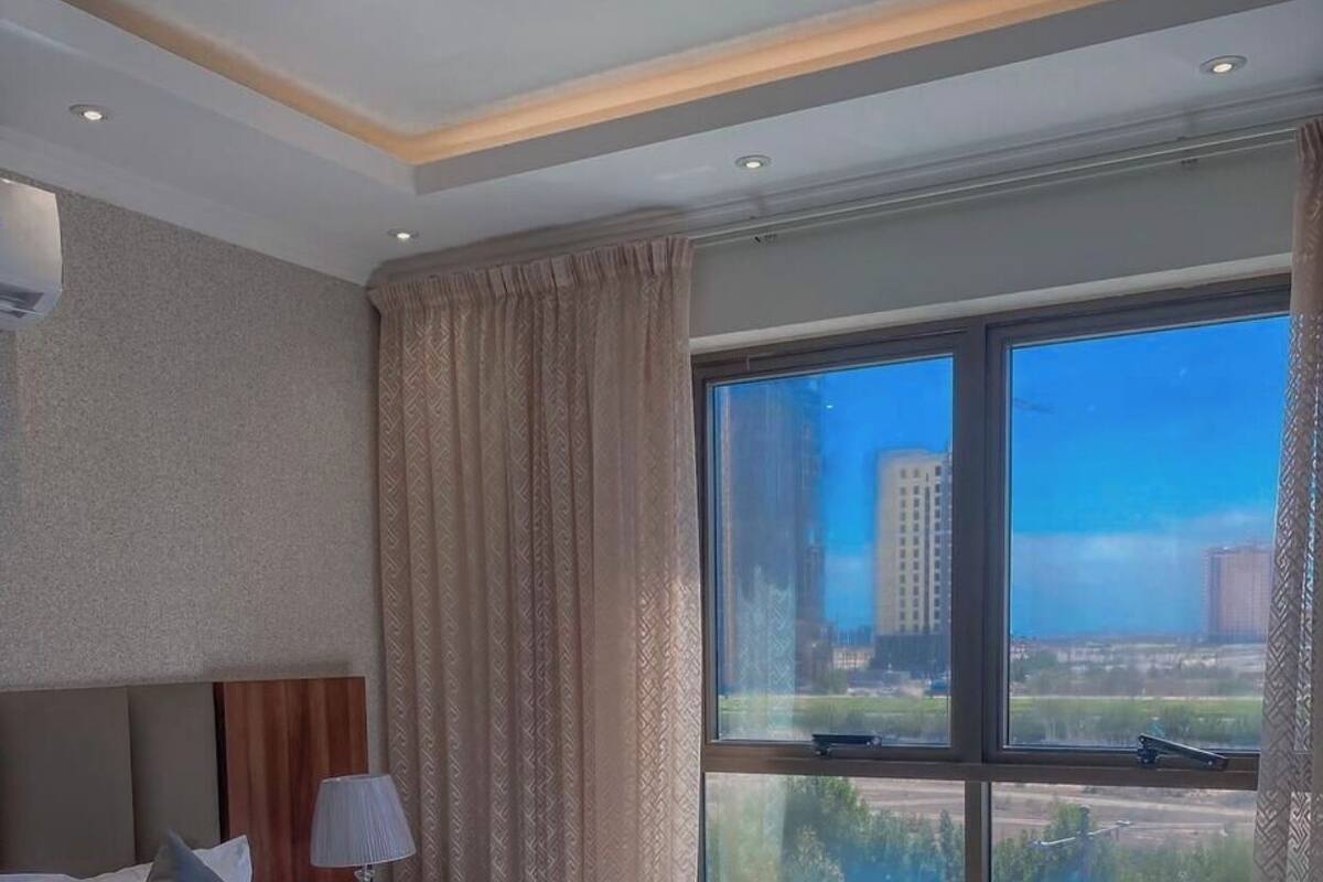 Habitación de hotel con una cama grande, una mesita de noche con lámpara y una ventana con vistas a la ciudad.