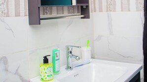 Et badeværelse med en hvid vask, et spejl og toiletartikler.