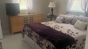 A bedroom with a bed, a TV, a dresser, a lamp, and windows with sheer curtains. - Poolside Cozy 2 bedroom pet friendly perfect getaway (Port Charlotte)