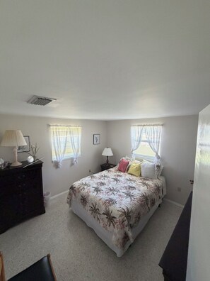 A bedroom with a bed, two bedside tables, a dresser, and two windows with curtains. - Poolside Cozy 2 bedroom pet friendly perfect getaway (Port Charlotte)
