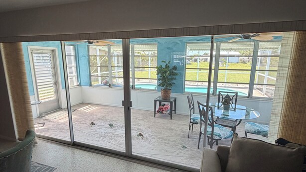 A room with a sliding glass door leading to a patio with a pool, outdoor furniture, and a ceiling fan. - Poolside Cozy 2 bedroom pet friendly perfect getaway (Port Charlotte)