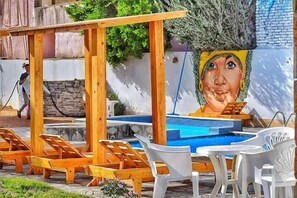 A poolside area with wooden lounge chairs, a white table, and a mural on the wall.