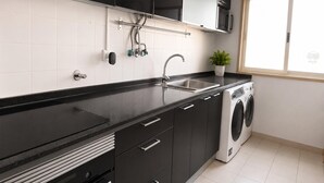 A modern kitchen with black cabinets, a stainless steel sink, a built-in washing machine, and a window providing natural light. - Spacious Lisbon Apartment With 4 Bedrooms (Lisbon)
