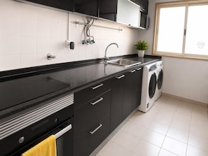 A modern kitchen with black cabinets, a stainless steel sink, a built-in washing machine, and a window providing natural light. - Spacious Lisbon Apartment With 4 Bedrooms (Lisbon)