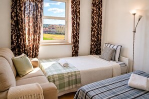 Een slaapkamer met een bed, een bank, een nachtkastje, een lamp en een raam met gordijnen.