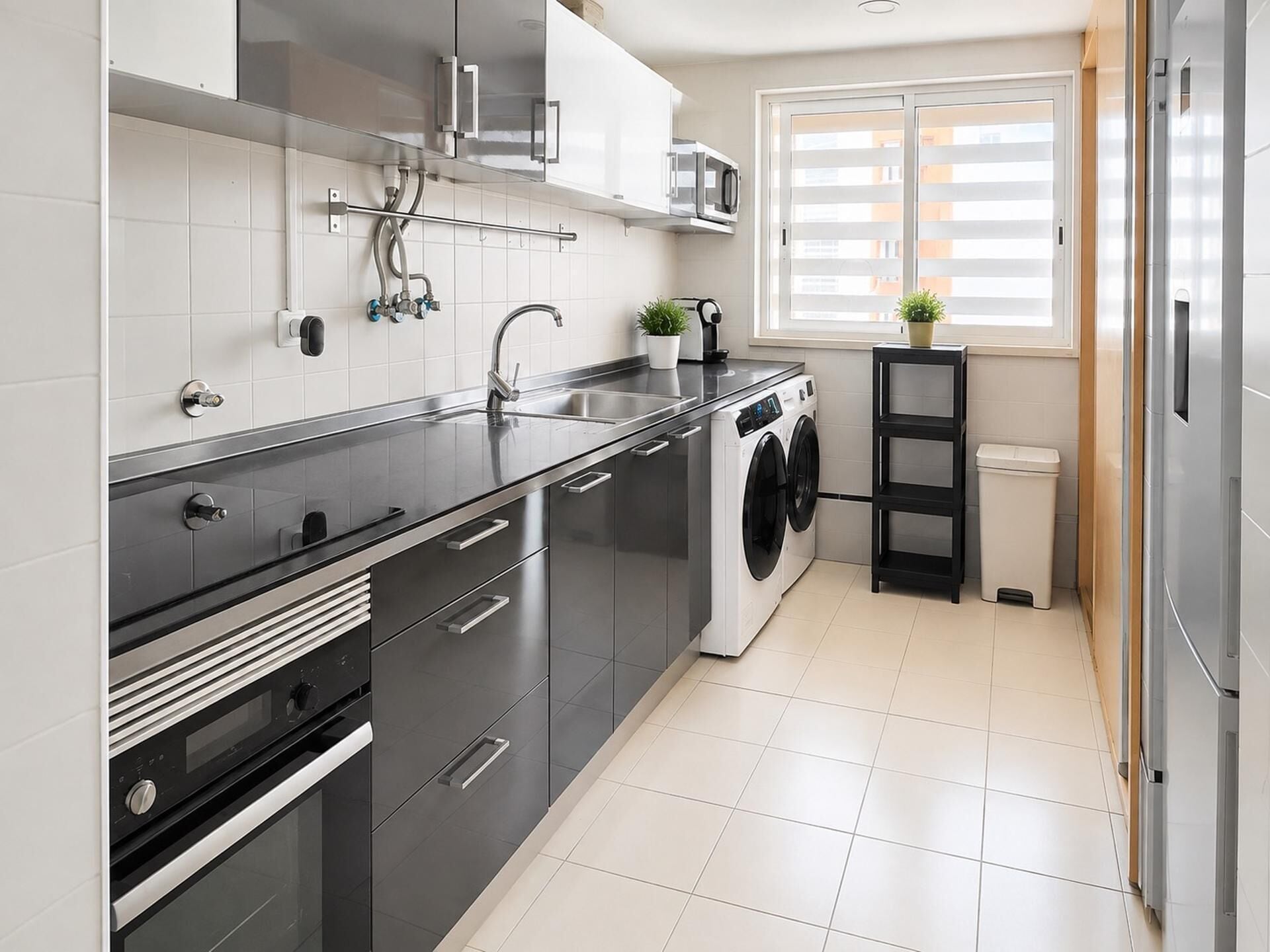 A modern kitchen with a built-in washing machine, stainless steel appliances, and a window with blinds.